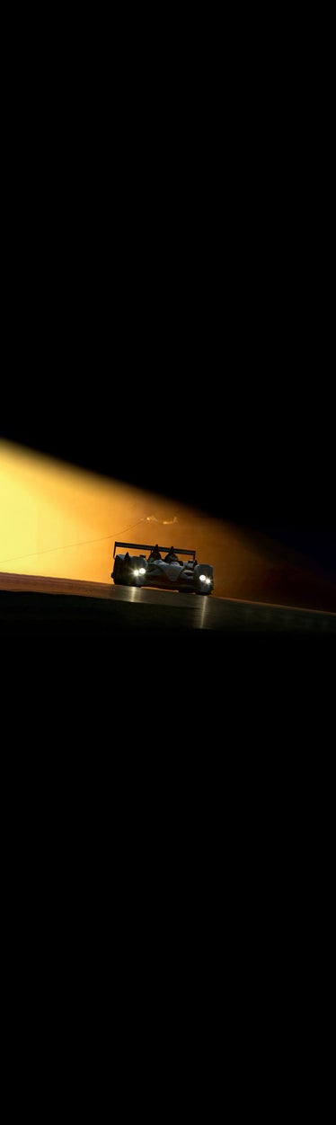 Front-view of an Audi racing vehicle in a darkened room with its headlights on.