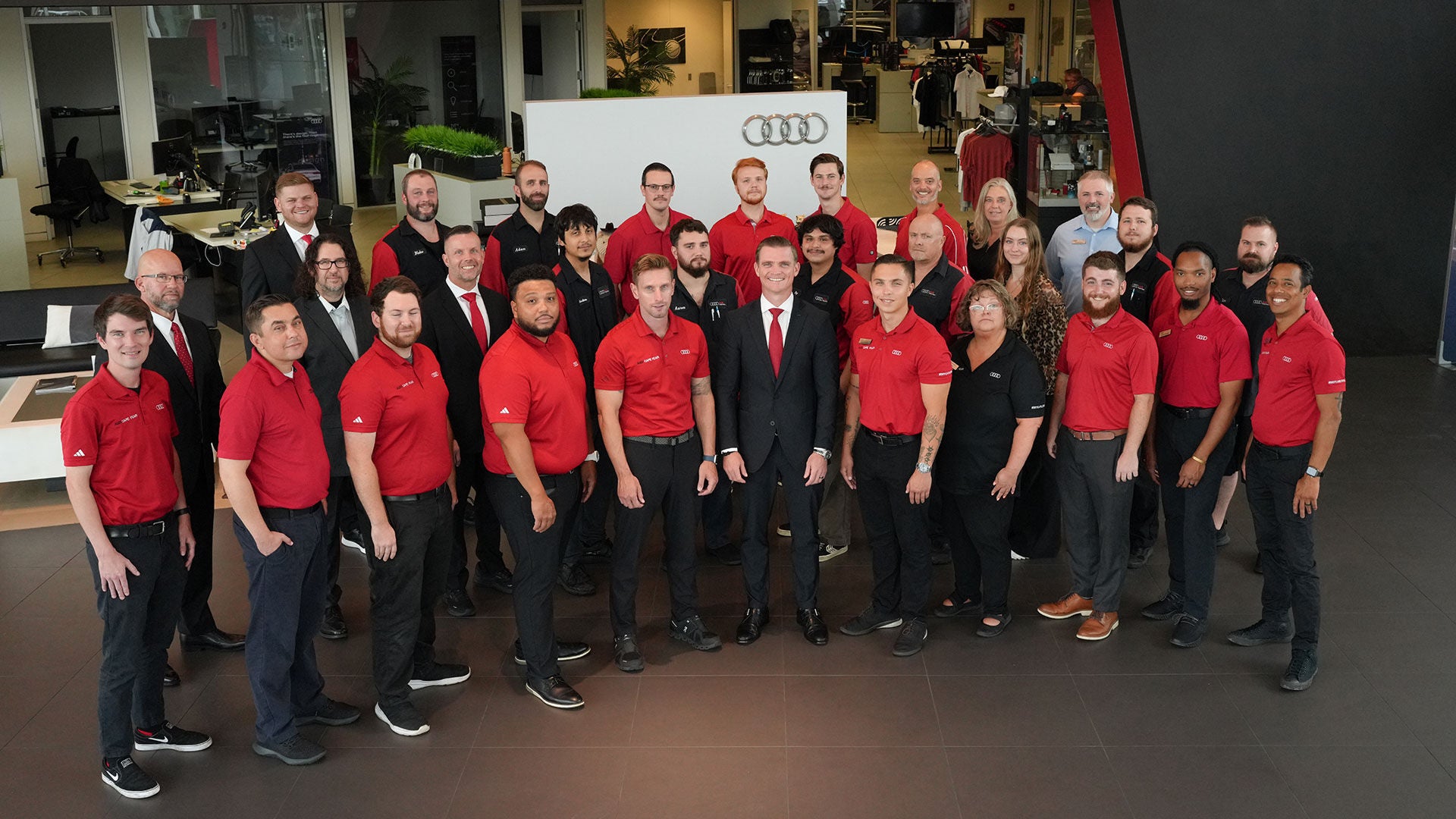 Audi sales specialist walking with a customer through the showroom. The sales specialist is handing the customer a key fob for an Audi vehicle.
