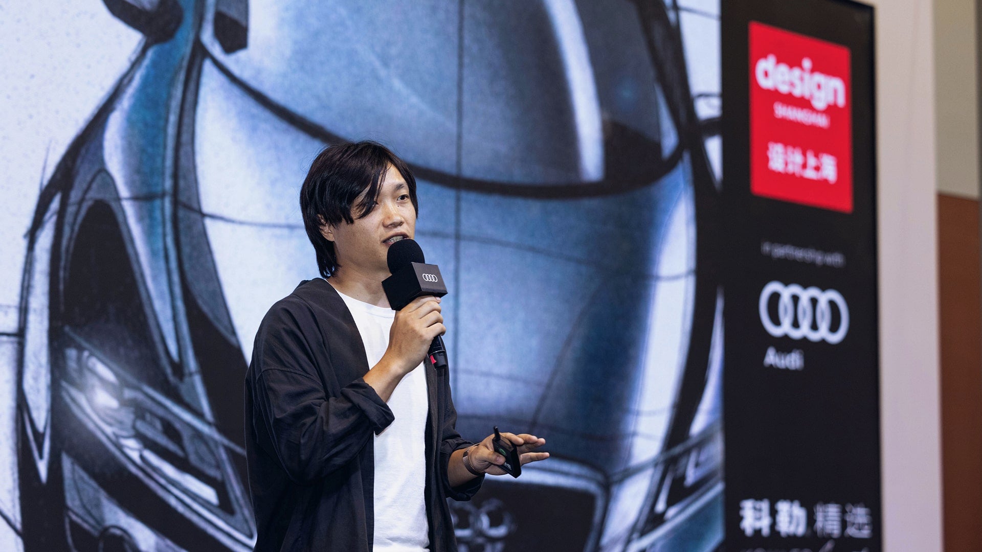 Person speaking on stage with a microphone at the Audi installation at Design Shanghai fair. 