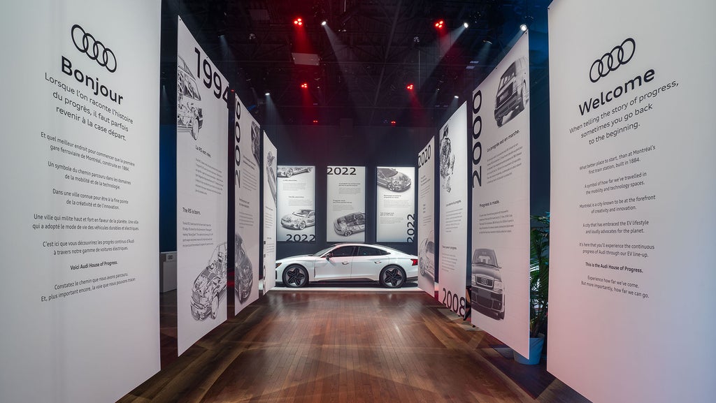 View of a long corridor with the Audi House of Progress installation along the walls, leading towards an Audi vehicle.