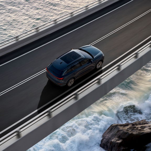 Aerial view of the Audi Q6 e-tron accelerating on an oceanside road.