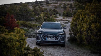 Front view of the 2025 Audi Q5 driving on a gravel road in a forested area.