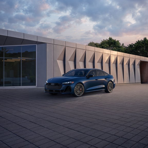 Three-quarter front view of the all-new Audi A5 parked by a modern building.