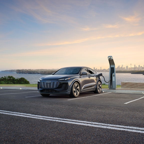 Vue de trois quarts avant d'une Audi Q6 Sportback e-tron grise garée et en charge au bord de l'eau.