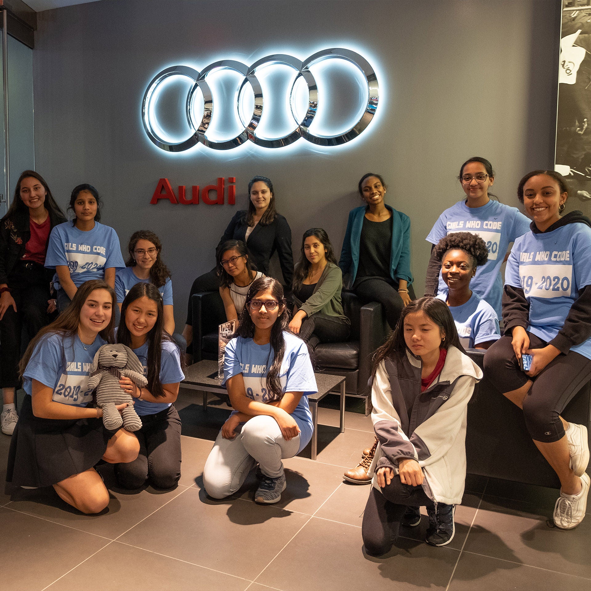 A group of girls posing in front of an Audi logo.