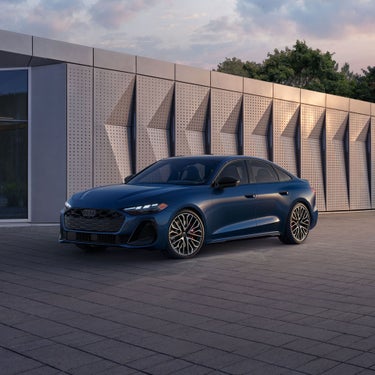 Three-quarter front view of the all-new Audi A5 parked by a modern building.