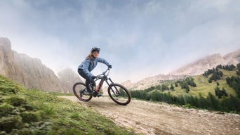A woman performing a turn with her Audi electric mountain bike, with a mountainous landscape behind.