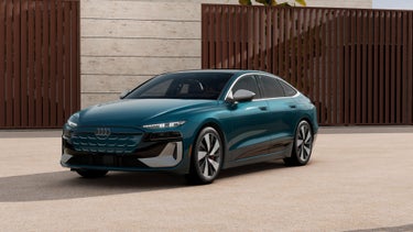 Three-quarter front view of the Audi S6 e-tron parked by a modern home.