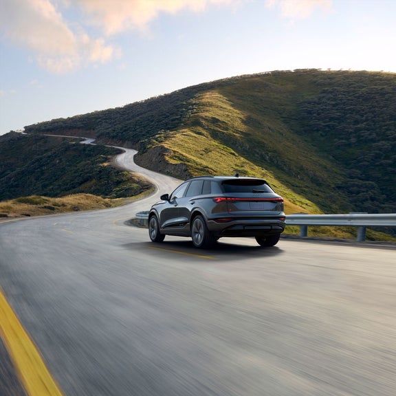 Plan arrière de trois quarts d’un Audi SQ6 e-tron gris qui accélère sur une colline.