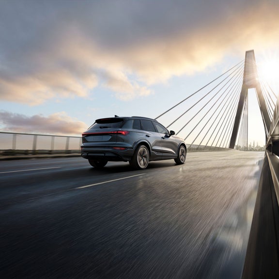 Plan arrière de trois quarts d’un Audi SQ6 e-tron gris qui accélère sur un pont.