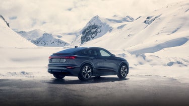 Three-quarter rear view of the Audi Q6 Sportback e-tron in front of a snowy mountainous landscape.