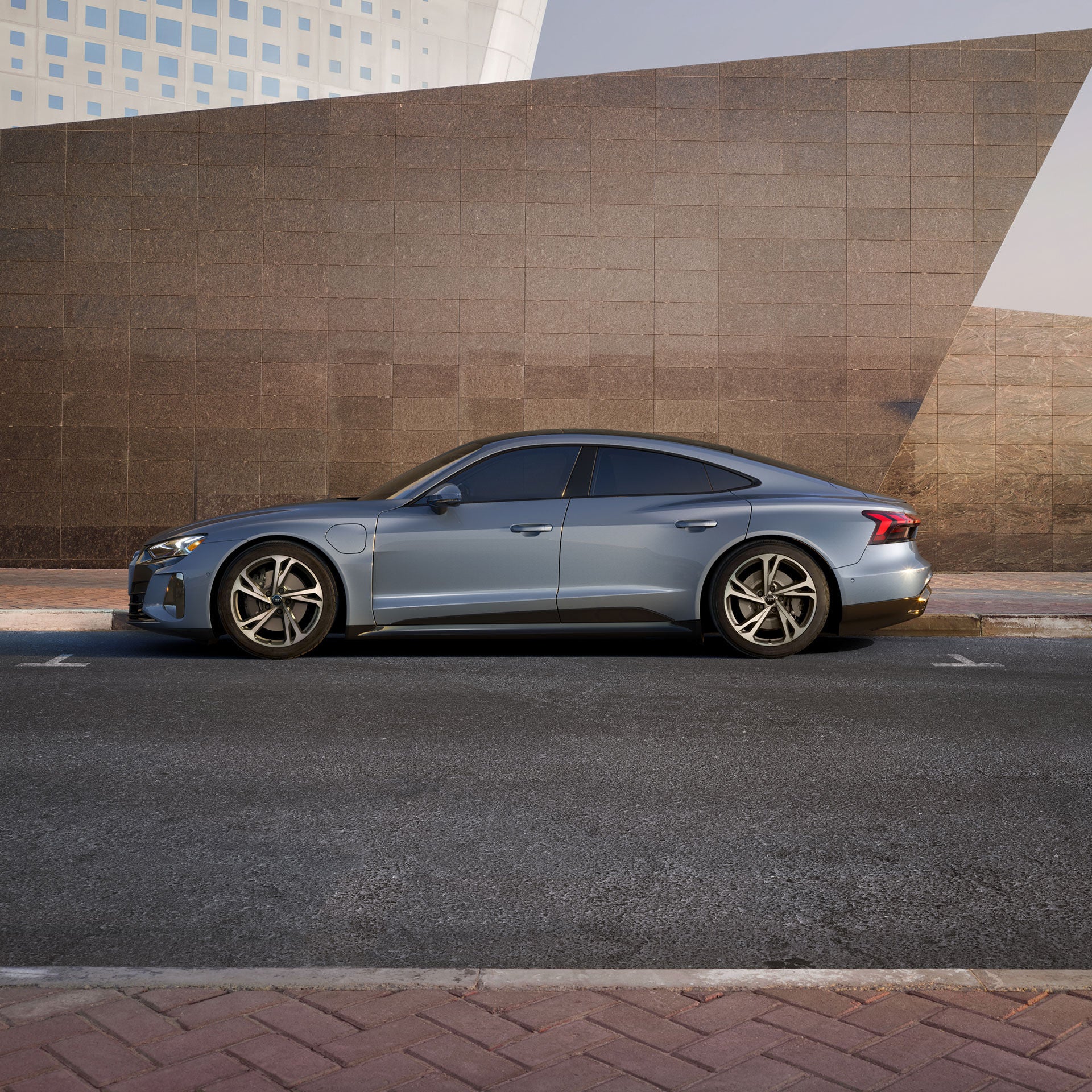 Side profile of an Audi e-tron GT parked in front of a tiled wall. 
