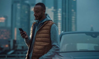 A man on his phone standing next to his Audi vehicle. 