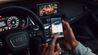 Close-up of a person using the myAudi app on their smartphone while seating in an Audi vehicle.