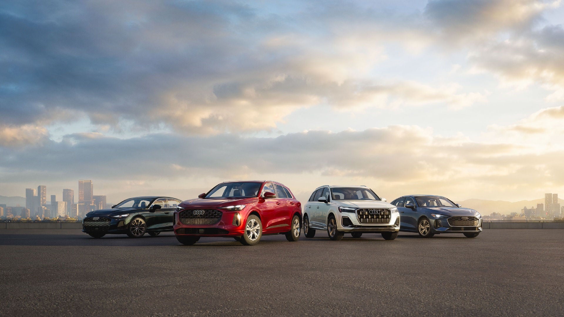 Four Audi vehicles parked side by side with a city skyline in the background.