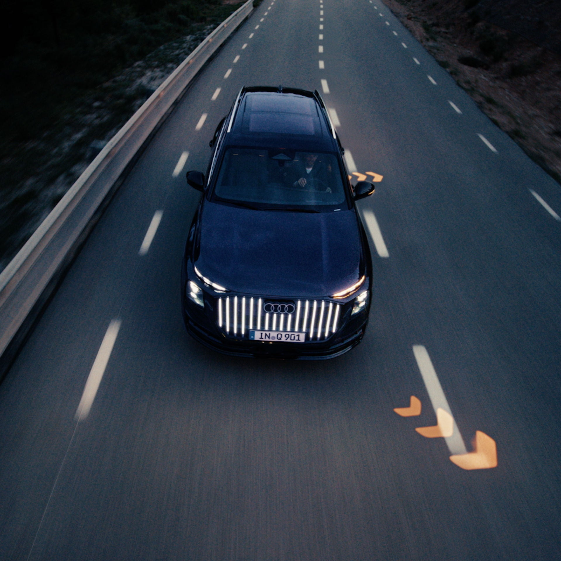 Aerial view of an Audi Q9 accelerating on a city road with turn signal indicators projecting on the road.