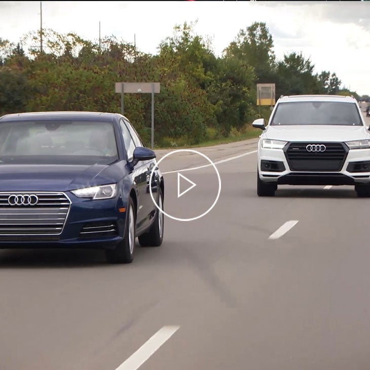 Front view of 2 Audi vehicles driving down a street.