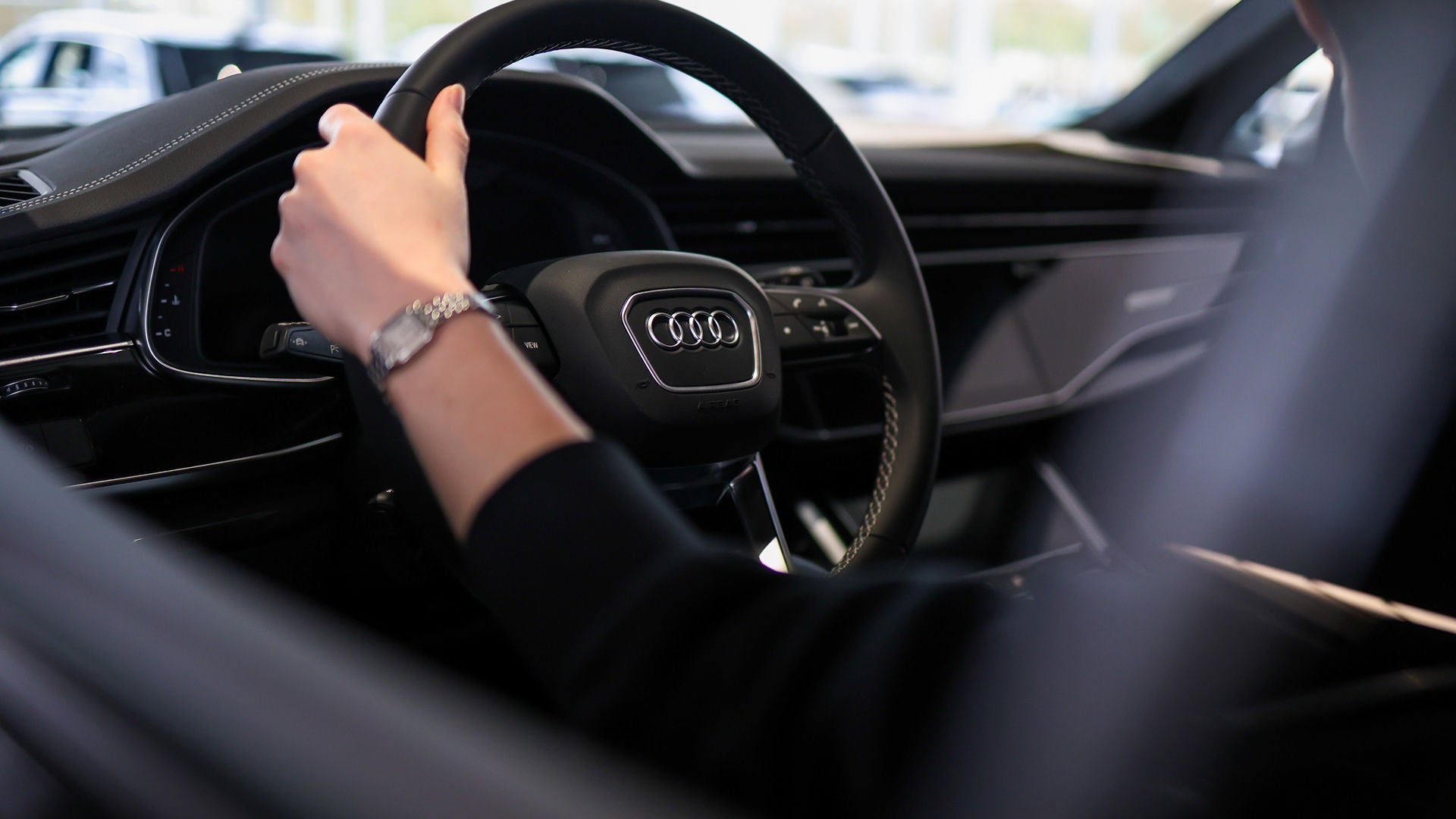 Audi sales specialist walking with a customer through the showroom. The sales specialist is handing the customer a key fob for an Audi vehicle.