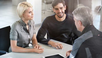 2 people sitting across an Audi employee in a dealership. 