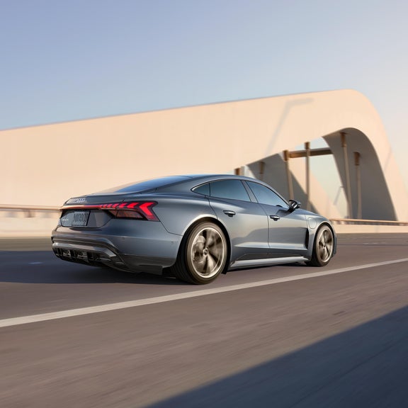 Profil latéral d’une Audi e-tron GT roulant sur un pont suspendu futuriste.