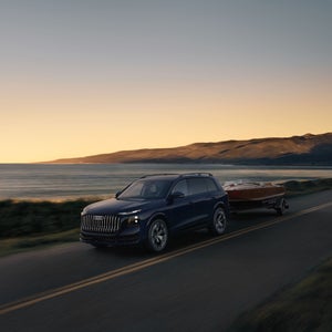 Exterior side view of an Audi 2027 Q9 driving and towing a boat.