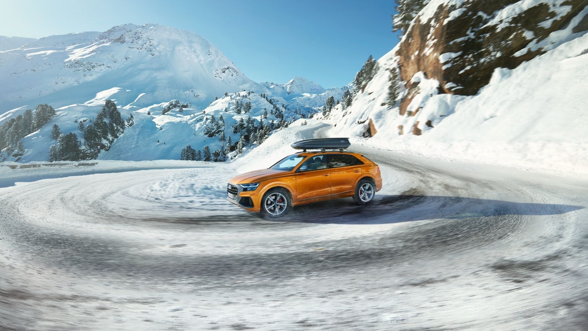 Picture of an orange Audi on a snowy mountain road