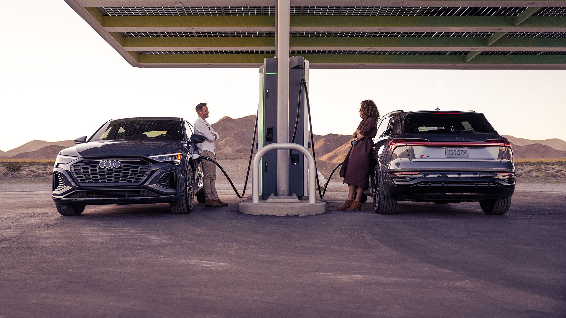 A man and a woman both charging their Q8 e-tron at an Electrify America charging station