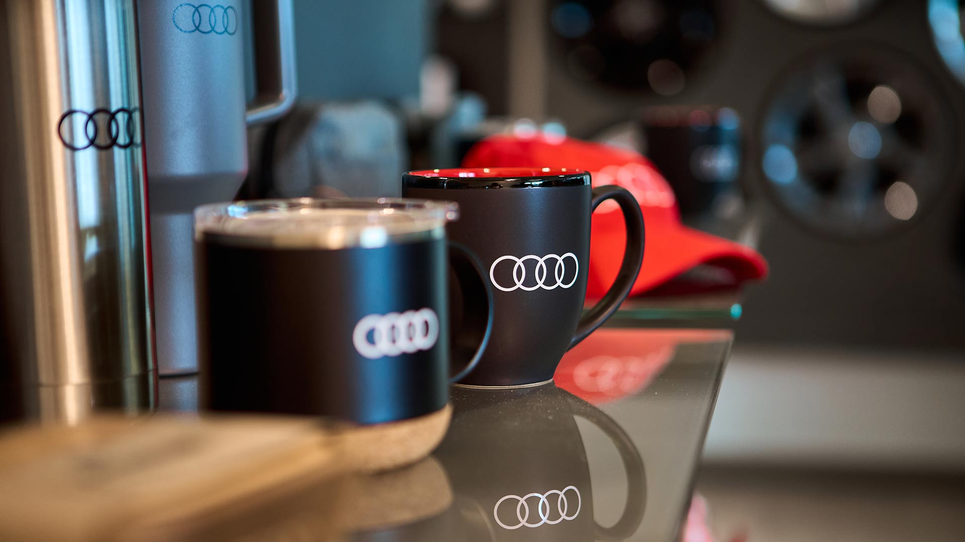 Produits dérivés Audi sur une table, comprenant une casquette, des tasses et des gobelets.