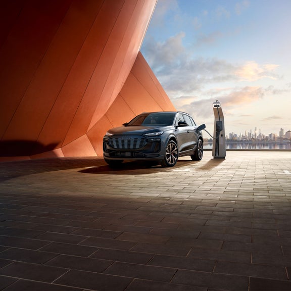 Plan avant de trois quarts d’un Audi SQ6 en cours de recharge près d’un bâtiment moderne.