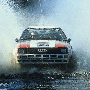 Front-view of the Audi quattro vehicle accelerating through a mud puddle.