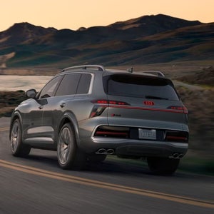 Grey Audi SQ9 towing a boat along a scenic lakeside road at sunset.