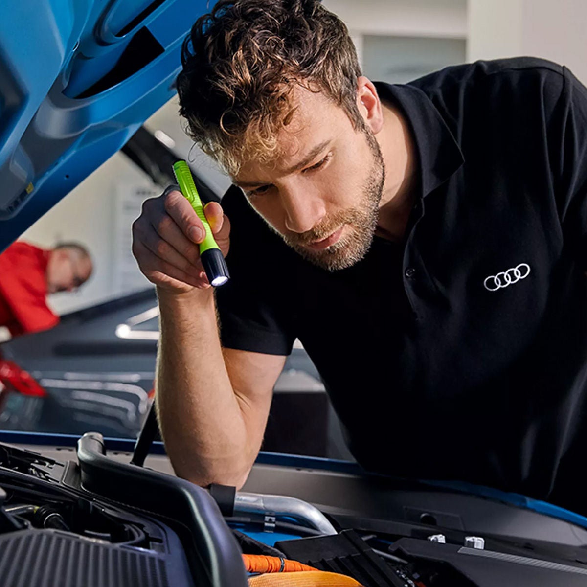 Audi Service tech shining a light on a vehicle engine