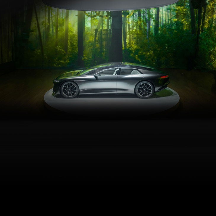 Side-profile of an Audi concept vehicle parked under a spotlight in a darkened room with a green background