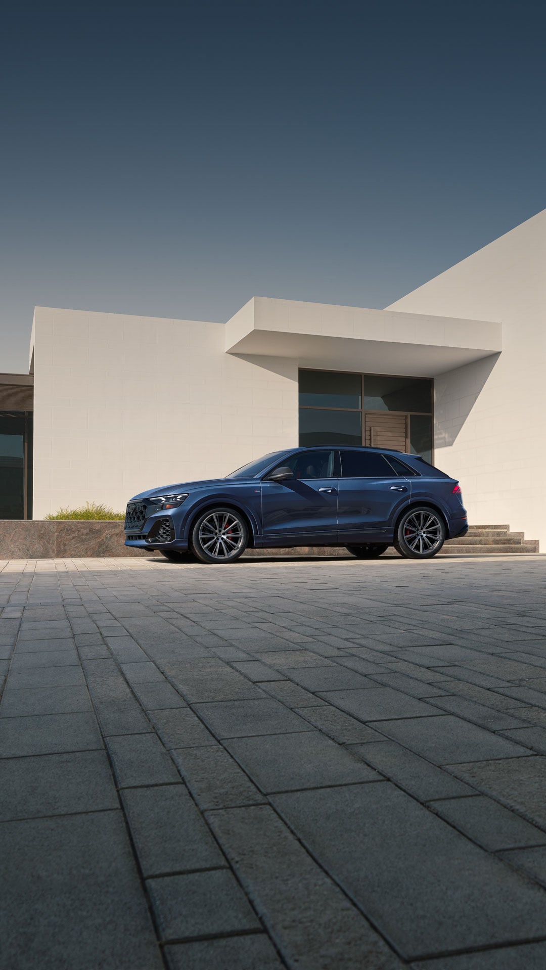 Side profile of the Audi Q8 parked in front of a modern home.