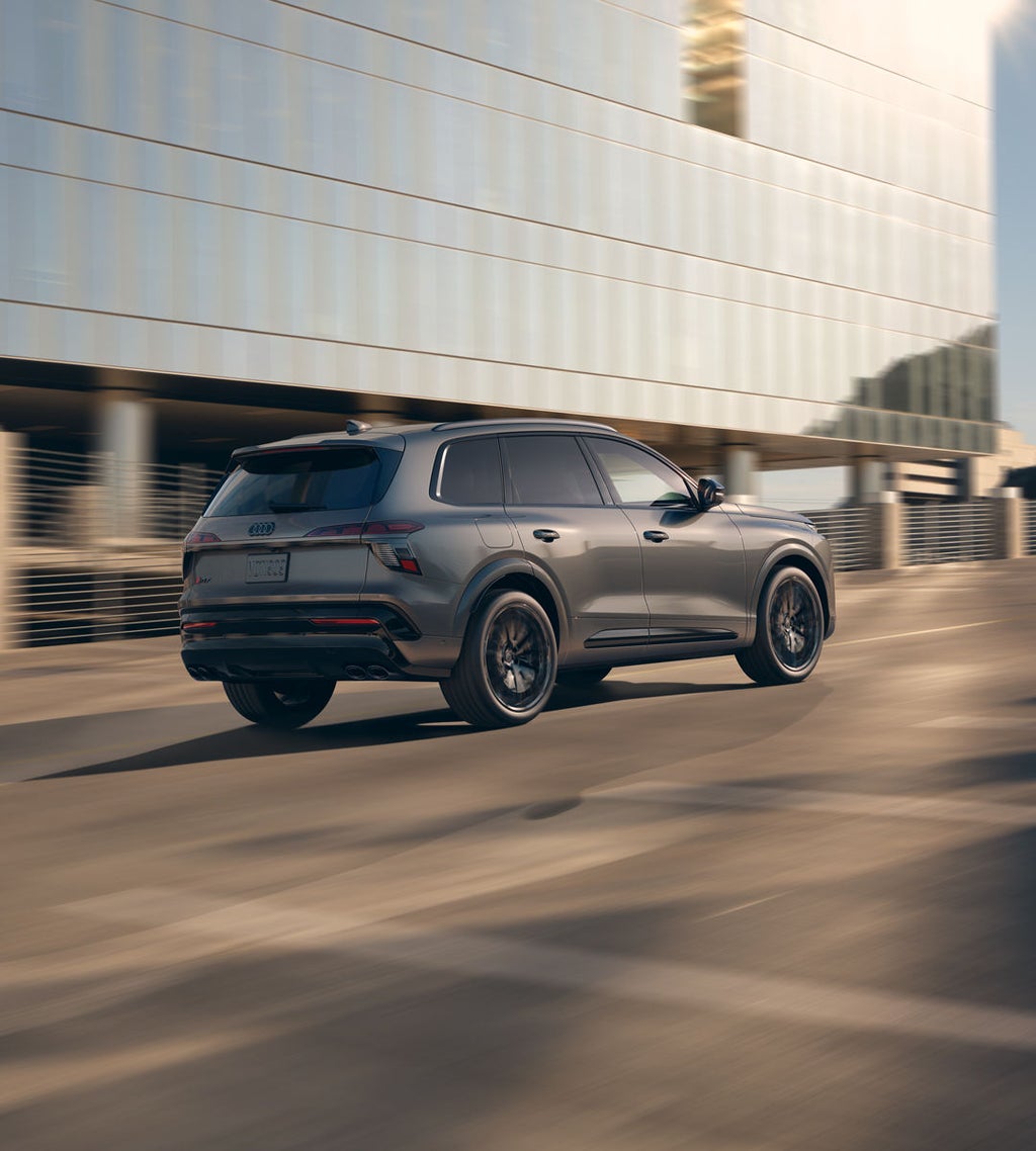 The Audi Q7 SUV, viewed from the rear at an angle on an urban street. In the background is a fully glazed office building.
