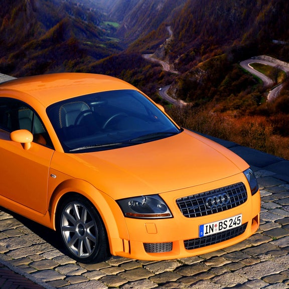 Front three-quarter view of an orange Audi TT Roadster parked high above a winding mountain road.