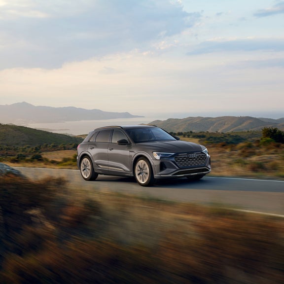 Three-quarter side profile of a gray Audi Q8 e-tron accelerating. 