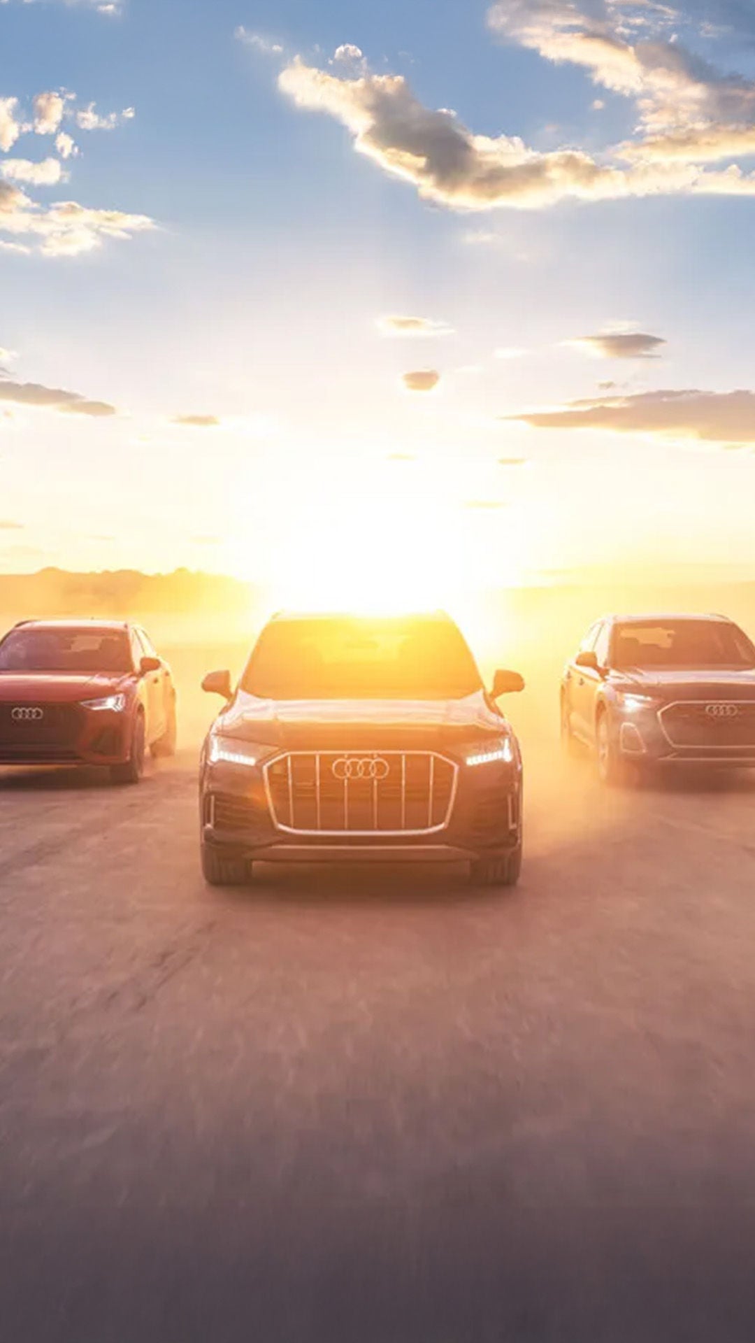 Three front profile Audi's accelerating with a sunset in the background.
