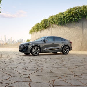 Side-view of the Audi Q6 Sportback e-tron parked with a cityscape in the background.