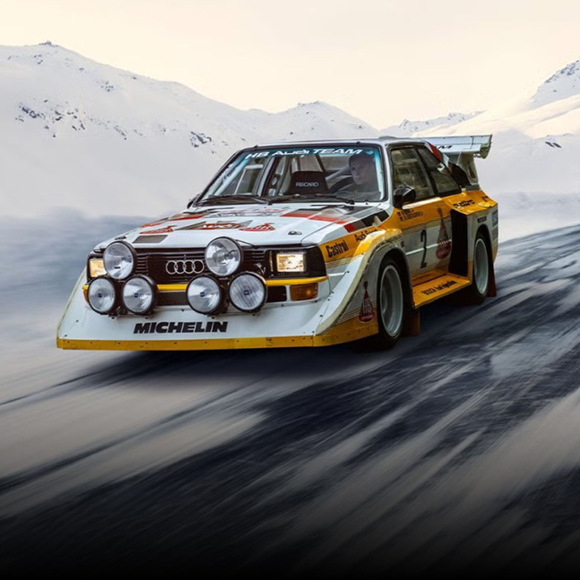 Three-quarter front-view of an Audi rally car accelerating on a snowy hill.