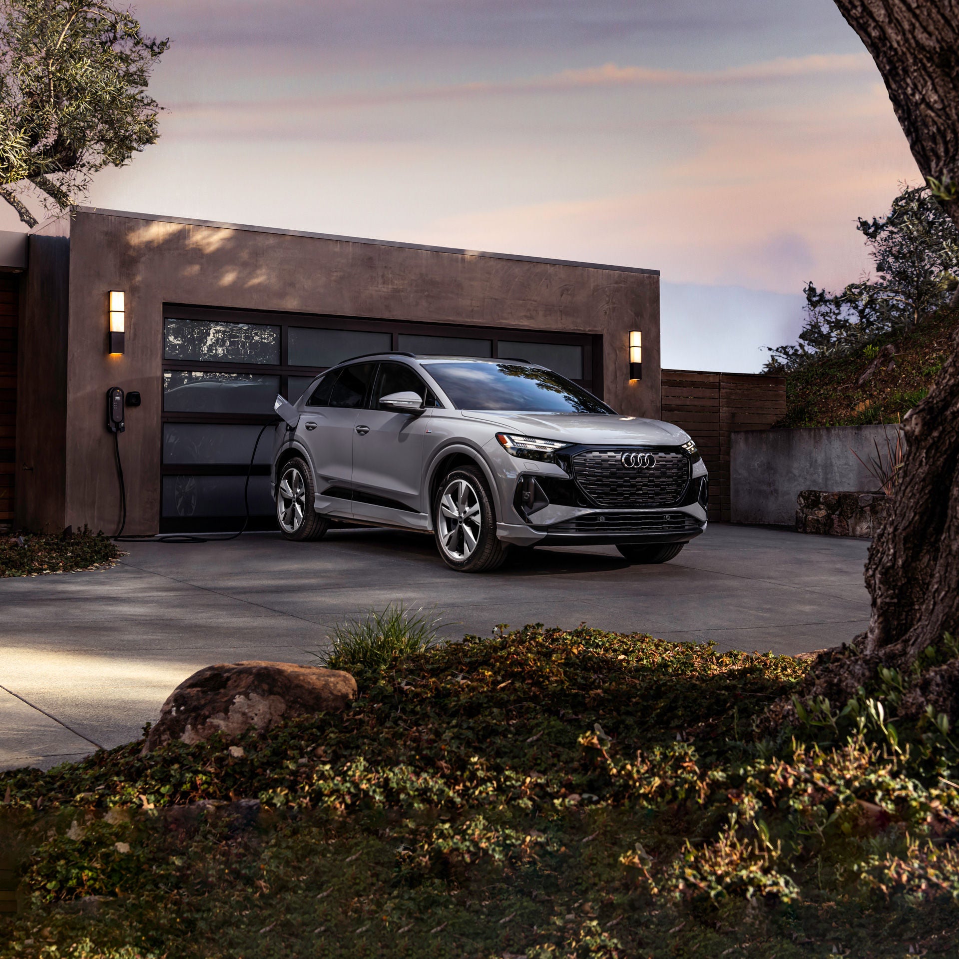 Three-quarter front-view of the Audi Q4 e-tron® charging in front of a person's home.