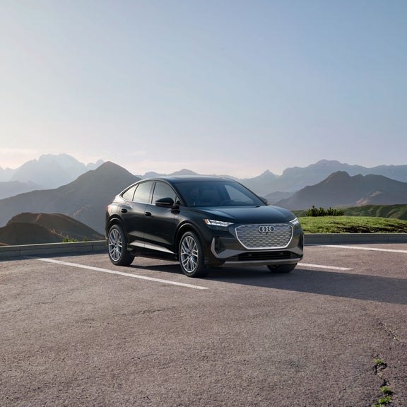 Three-quarter front view of a black Audi Q4 Sportback e-tron parked with a mountain range in the background.