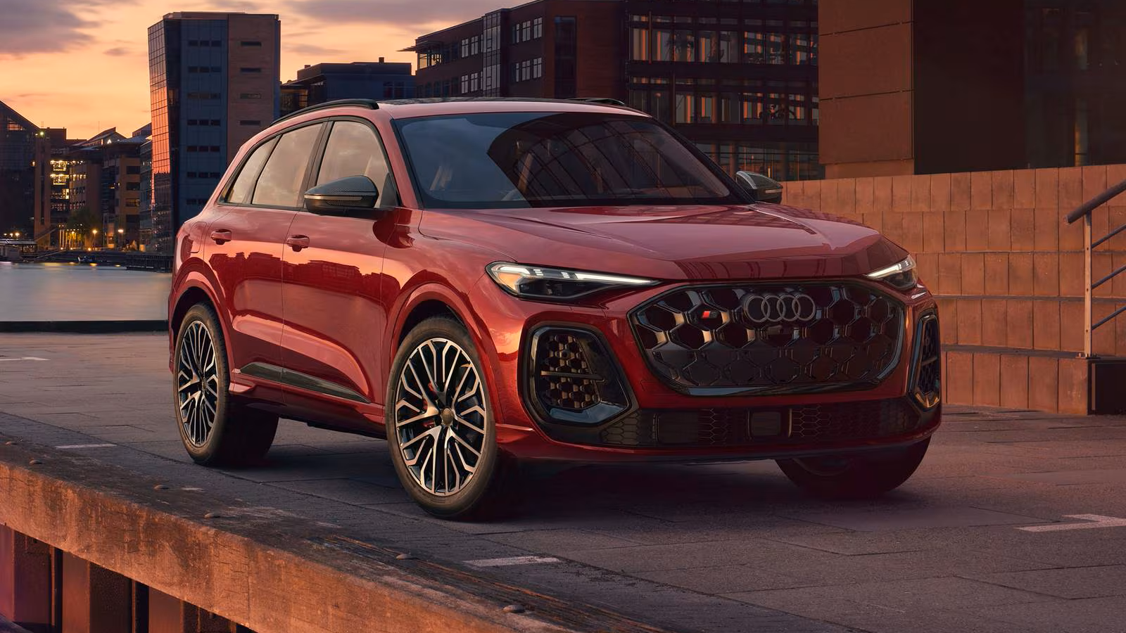 Red 2026 SQ5 car parked in front of a building with a sunset in the background. 