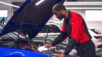 Mechanic leaning over an open hood, examining engine components during a diagnostic inspection