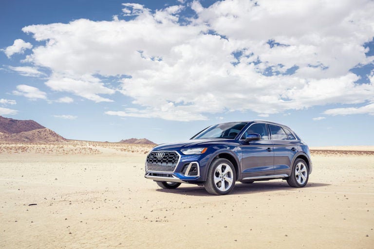 A blue Audi SUV parked in a desert landscape beneath a partly cloudy sky.
