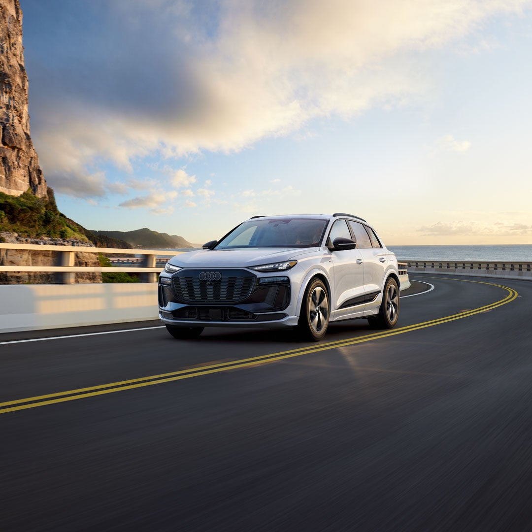 Three-quarter front view of the Audi Q6 e-tron accelerating on a hillside road.