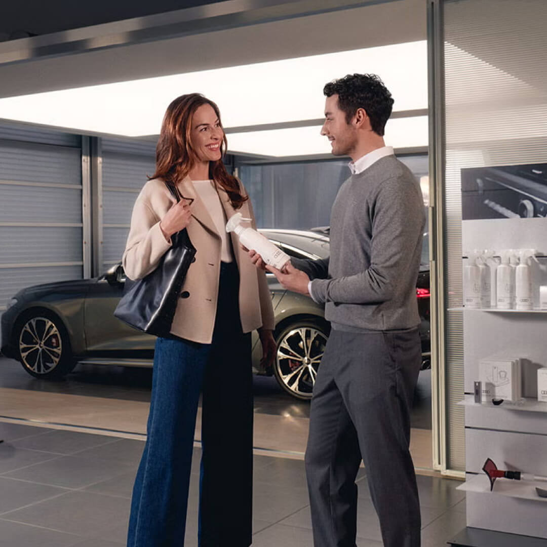 A woman smiles as an Audi Sales representative assists her in a dealership.