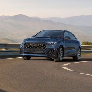 Three-quarter front view of the Audi Q8 accelerating on a mountainside road.