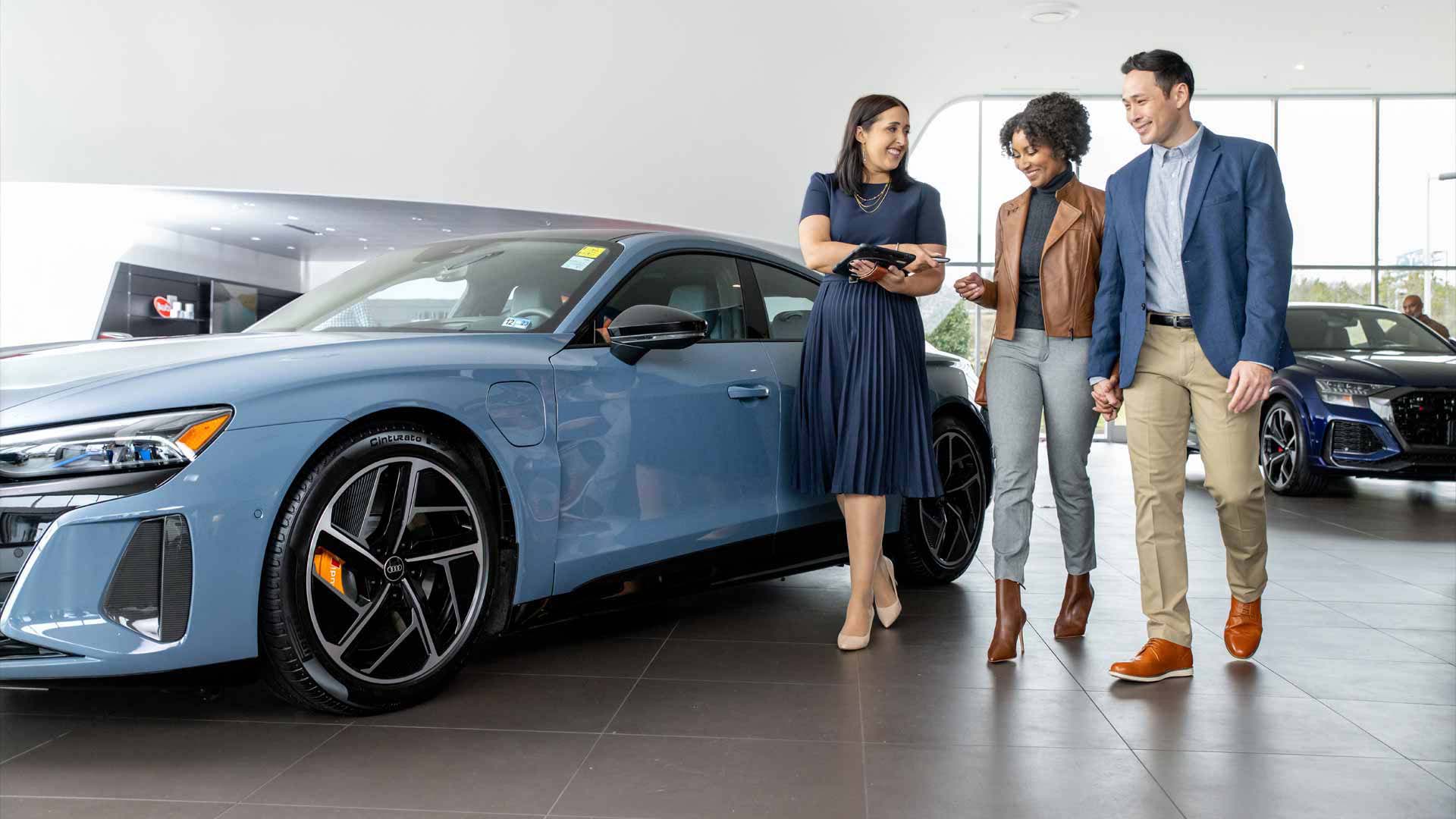Audi employee showing two people an Audi vehicle.