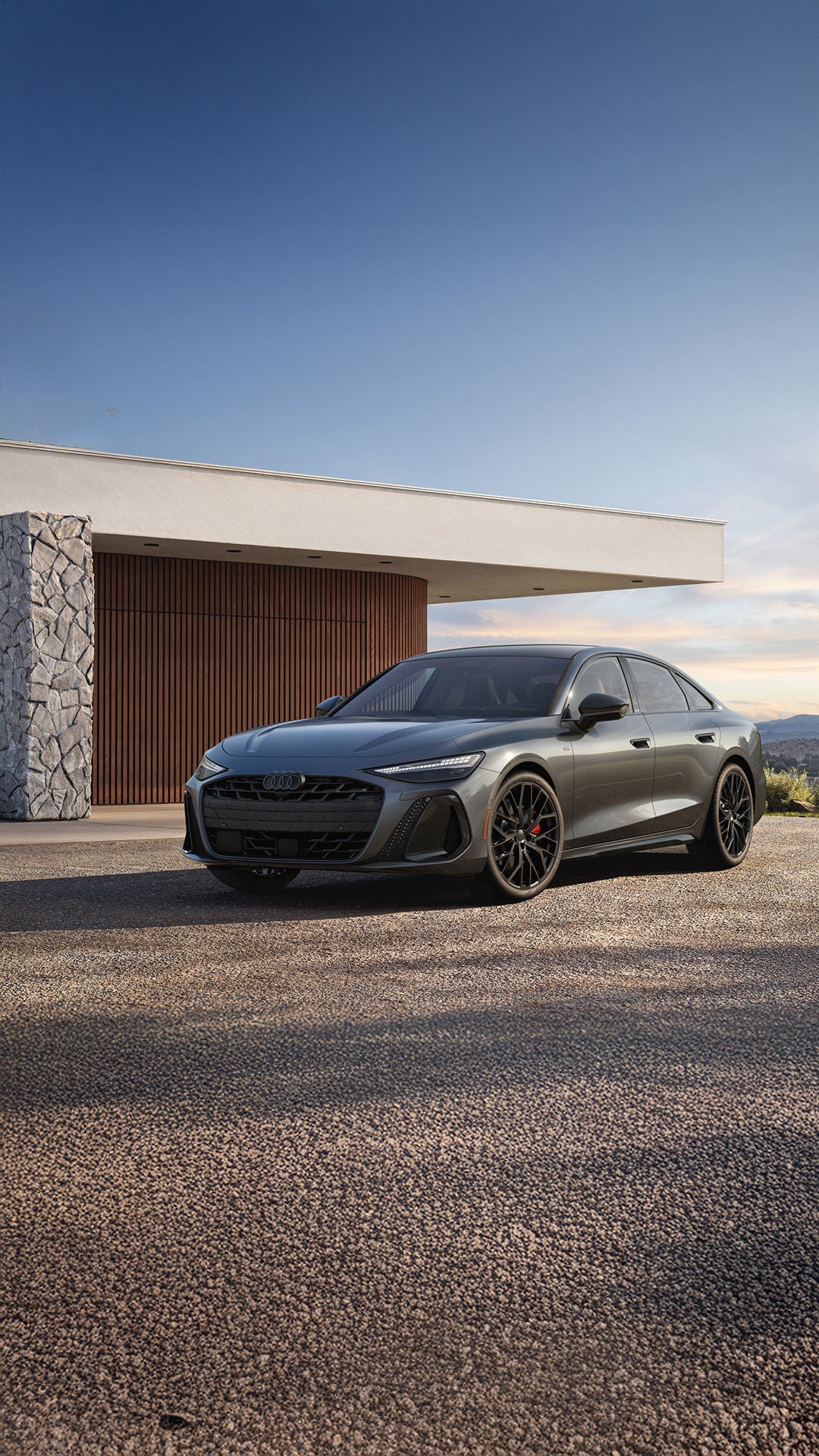 2026 Audi A6 trim level parked in front of a modern brick and wood home in a lush setting
